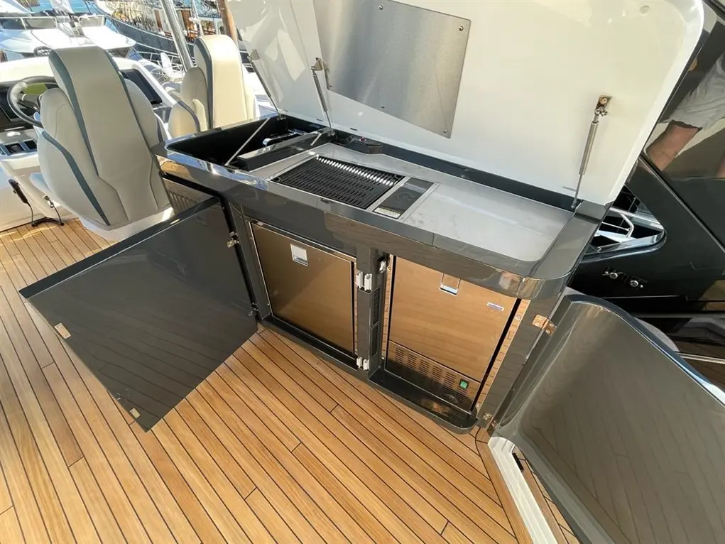 Modern boat outdoor kitchen with stainless steel grill, storage compartments, and wooden decking in bright sunlight.